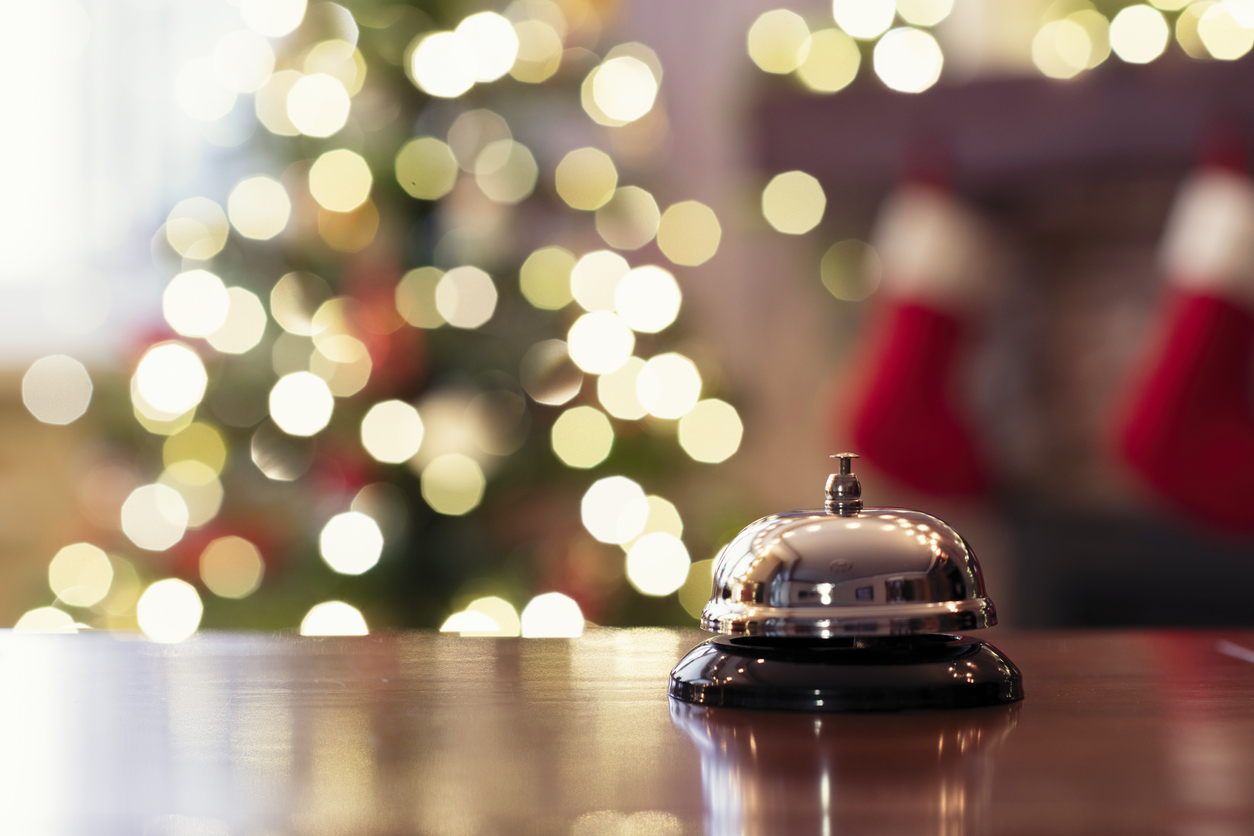 Christmas travel. Silver vintage bell on reception desk of guesthouse  and color shining garland on christmas tree on background. Hotel, restaurant.