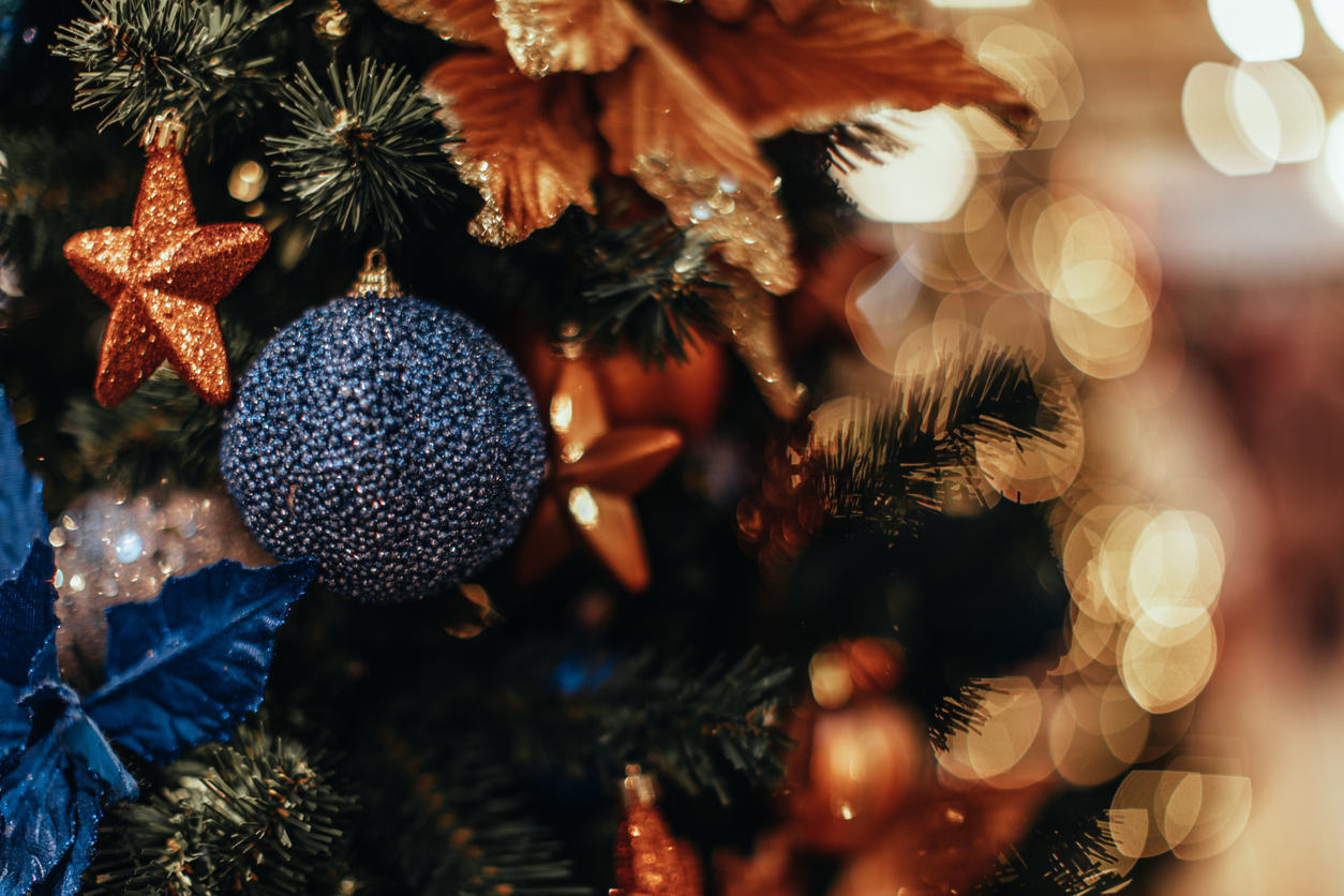 Bright blue Christmas ball hanging on the Christmas tree with garland lights.
