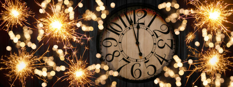 HAPPY NEW YEAR 2023 – Festive silvester New Year’s Eve Party celebration background panorama banner long – Golden yellow fireworks, sparklers and clock on rustic black wooden wall texture in the night