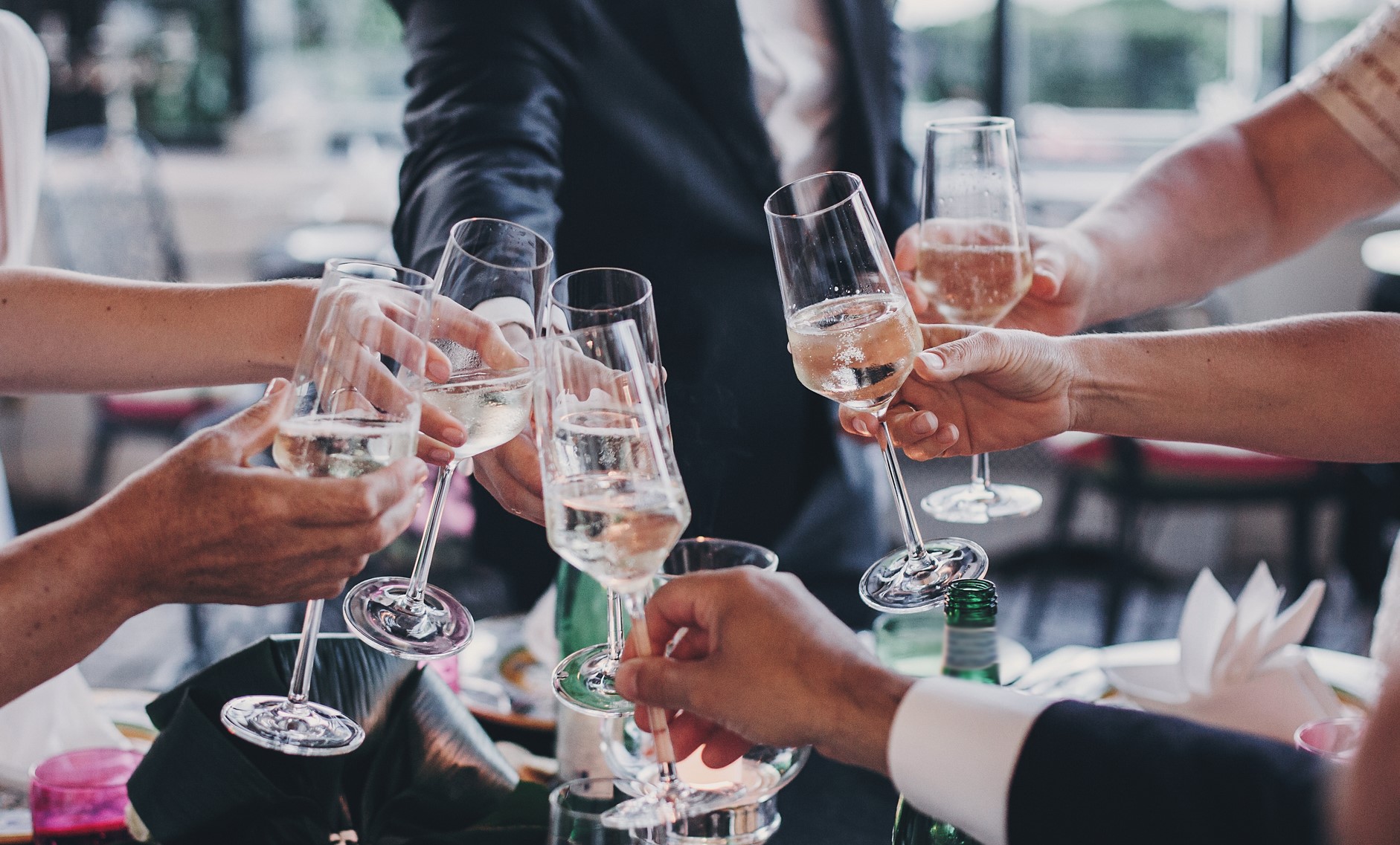 Group of people holding champagne glasses and toasting at wedding reception outdoors in the evening. Family and friends clinking glasses and cheering with alcohol at delicious feast celebration