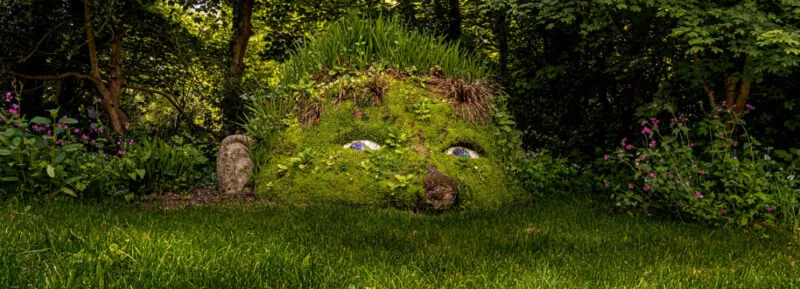 Eyes and a face surrounded by plants and moss on a rock formation in the Garden of Heligan