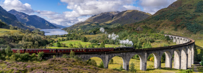 View of the Glenfinnan Railway Viaduct in Scotland surrounded by mountains and water.
