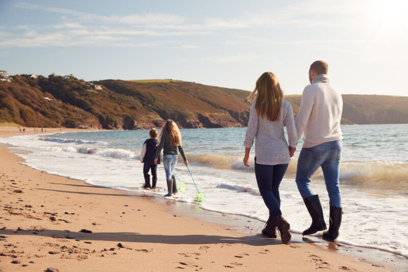 Rear,View,Of,Family,With,Fishing,Nets,Walking,Along,Shoreline